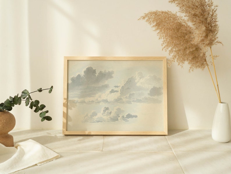 May include: A framed watercolor painting of a cloudy sky in shades of blue and gray. The painting is in a light wood frame and is hanging on a white wall.