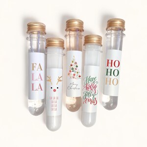 May include: Five clear glass tubes with gold lids and festive Christmas labels. The labels feature a reindeer, a Christmas tree, and the phrases "Fa La La", "Have a Holly Jolly Xmas", and "Ho Ho Ho".