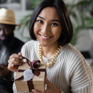 May include: A woman is holding a gift box wrapped in brown paper with a brown ribbon and a white tag that says "I am thankful for the small things".