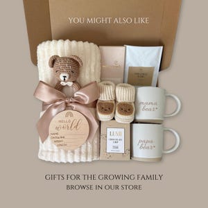 Puede incluir: Una caja de regalo que contiene una manta acanalada color crema con un sonajero de oso tejido a crochet marr&oacute;n, un disco de madera 'Hello World' para nacimiento, patucos color crema con caras de oso, dos tazas 'mama bear' y 'papa bear', caf&eacute; y chocolate.