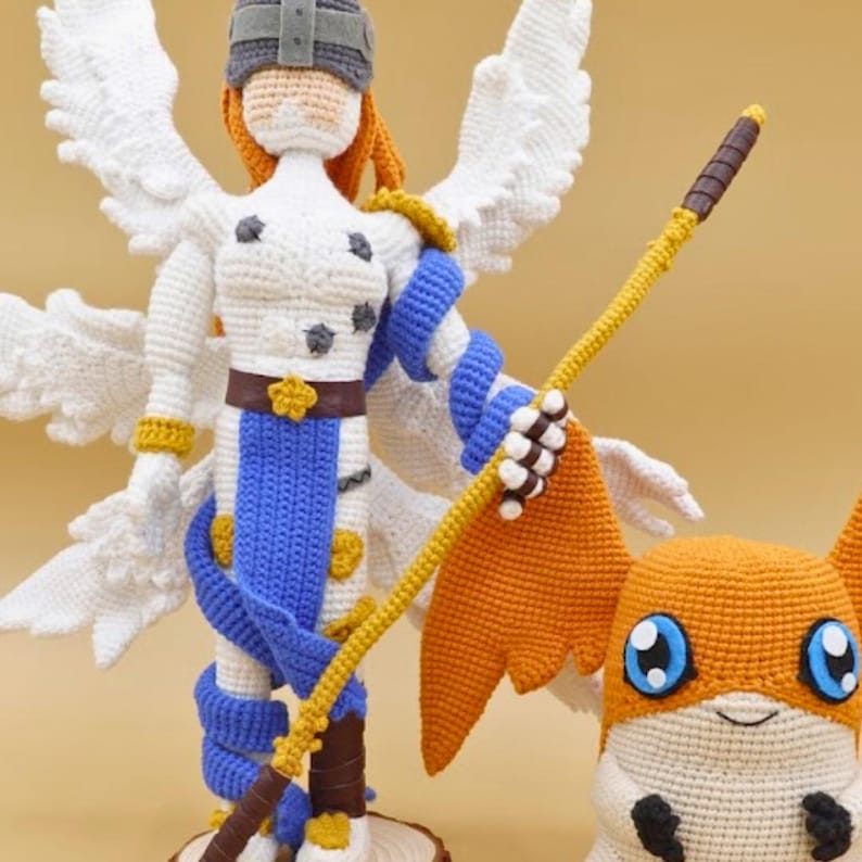 以下が含まれることがあります： 白い翼、青と白の鎧、槍を持ったキャラクターと、オレンジと白の生き物の手編みの編みぐるみ。 細かいステッチと鮮やかな色で作られたこれらの人形は、ファンタジーをテーマにしています。