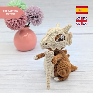 May include: Crocheted amigurumi toy of a brown and white Pokemon character, "Aegislash", with a bone-like sword in its hand. The toy is sitting on a light wood surface.  PDF PATTERN ESP/ENG