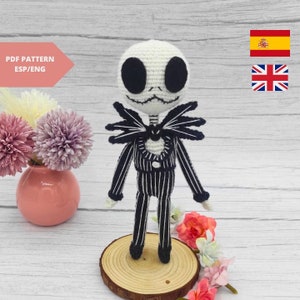 Op de afbeelding: Een gehaakte amigurumi-pop van Jack Skellington uit The Nightmare Before Christmas. De pop draagt ​​een zwart-wit gestreept pak met een zwarte strik. De pop staat op een houten voet.
