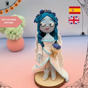 May include: A handmade crochet doll of a character with blue skin, hair, and a white dress with blue accents. The doll holds a small bouquet and stands on a wooden base. The doll is a Halloween or gothic theme.
