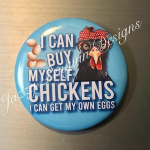 May include: A round, light blue button with the text "I CAN BUY MYSELF CHICKENS I CAN GET MY OWN EGGS." The button features a cartoon chicken wearing glasses and a red polka dot bandana, with a cluster of eggs.