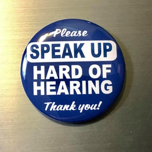 May include: A round, blue button with white text. The text reads "Please SPEAK UP HARD OF HEARING Thank you!" The button is glossy and has a slight reflection.