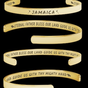 Può includere: Braccialetti a polsino in metallo color oro con testo inciso. Un braccialetto recita "JAMAICA" e un altro recita "ETERNAL FATHER BLESS OUR LAND GUIDE US WITH TH". I braccialetti hanno un design semplice ed elegante.
