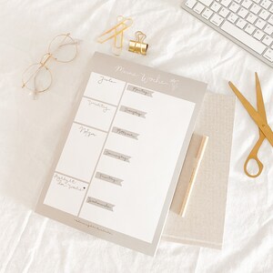 Pu&ograve; includere: Un planner settimanale con sfondo grigio e testo bianco. Il planner ha una sezione per ogni giorno della settimana, a partire dal luned&igrave; e terminando con la domenica. Il testo "Meine Woche" &egrave; in cima al planner.