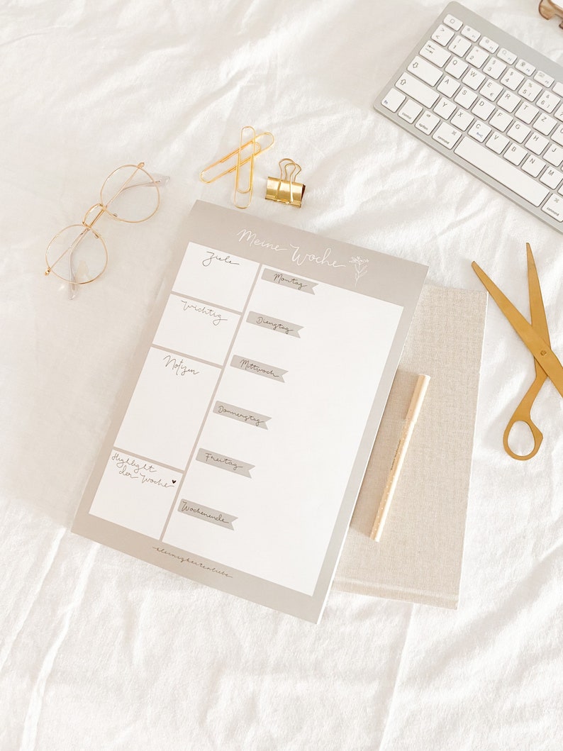 Pu&ograve; includere: Un planner settimanale con sfondo grigio e testo bianco. Il planner ha una sezione per ogni giorno della settimana, a partire dal luned&igrave; e terminando con la domenica. Il testo "Meine Woche" &egrave; in cima al planner.