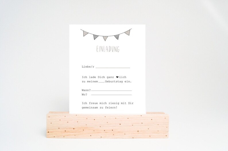 May include: A printable birthday invitation card with a string of flags at the top and the text "EINLADUNG" in black. The text reads "Liebe/r, Ich lade Dich ganz herzlich zu meinem. Geburtstag ein. Wann? Wo? Ich freue mich riesig mit Dir gemeinsam zu feiern!"