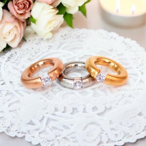 May include: Three simple wedding bands with a single clear stone set in each. The bands are gold, silver, and rose gold.