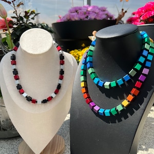 May include: Two necklaces made of colourful square beads. One necklace is red, black and silver. The other necklace is a rainbow of colours.