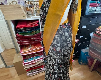 May include: A black and white saree with a floral pattern and a yellow border. The saree is draped on a mannequin.