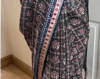 May include: A dark green and pink patterned saree with a decorative border. The saree is draped, showcasing the intricate design and color palette. The border features a blue and gold trim.