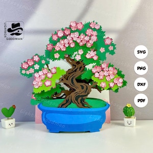 Könnte beinhalten: Ein Papier-Bonsai-Baum mit braunem Stamm, grünen Blättern und rosa Blüten, in einem blauen Topf. Der Baum ist von kleinen Kaktusfiguren umgeben. Das Bild enthält das Logo "Lightbox Goodman" und Dateityp-Symbole.