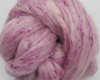 May include: A close-up of a bundle of pink and white wool fibre with purple and silver glitter throughout.