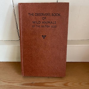 May include: A vintage book titled "The Observer's Book of Wild Animals of the British Isles." The cover is a textured, reddish-brown color with the title in dark text. A small, triangular emblem is at the bottom.