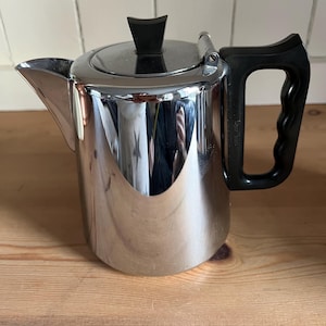 May include: A silver teapot with a black handle and lid. The teapot has a shiny, reflective surface.
