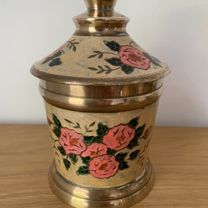 May include: A brass jar with a lid, decorated with pink and green roses. The jar has a gold finish and is hand-painted.