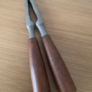 May include: A silver nutcracker with wooden handles. The nutcracker has a serrated edge and a hinged jaw.