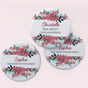 Peut inclure: Trois badges ronds blancs avec des motifs floraux et du texte. Les badges présentent des fleurs roses, des feuilles vertes et les noms "Christelle" et "Sophie" avec le titre "aide médico psychologique".
