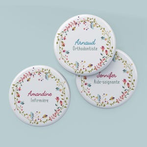 Peut inclure: Trois badges ronds blancs avec des motifs de couronnes florales. Chaque badge porte un nom et une profession de couleur différente. Les noms sont "Amandine, Arnaud et Jennifer". Les professions sont "Infirmière, Orthodontiste et Aide-soignante".