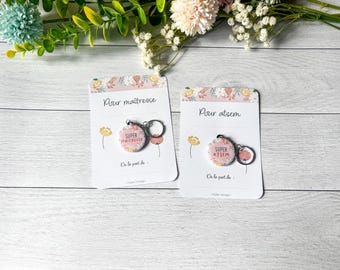 May include: Two keychains with floral designs and the text "SUPER MAITRESSE" and "SUPER ATSEM" on cards that read "Pour maîtresse" and "Pour atsem". The keychains have a silver ring and a pink floral design.