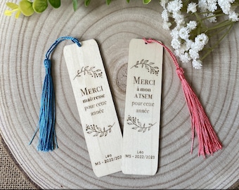 May include: Two wooden bookmarks with tassels. One has a blue tassel, the other a pink tassel. Both have the words "MERCI maitresse pour cette année" and "MERCI à mon ATSEM pour cette année" engraved, along with floral designs and the name "Leo" and dates.