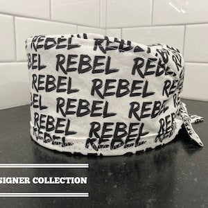 May include: White scrub hat with a black and white print of the word "Rebel" repeated across the fabric. The hat has a tie on the back.