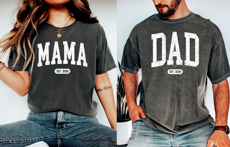May include: Two gray t-shirts with white text. The shirt on the left says "MAMA EST. 2024" and the shirt on the right says "DAD EST. 2024".