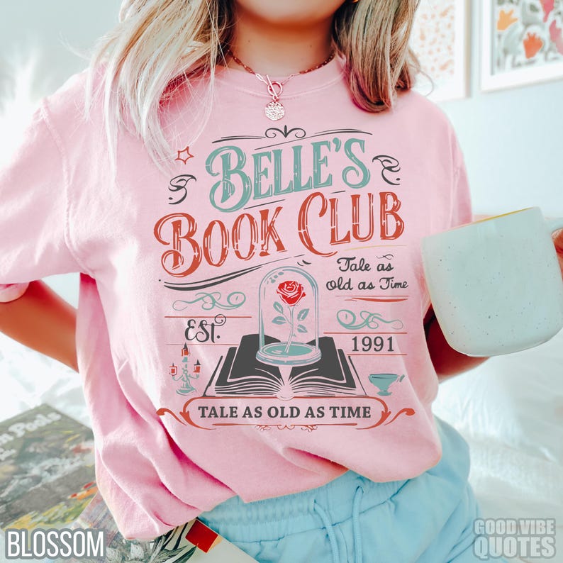 May include: Pink t-shirt with the text "Belle's Book Club" in a vintage design. The design includes a rose in a glass dome, the words "Tale as old as Time," and the year "1991."