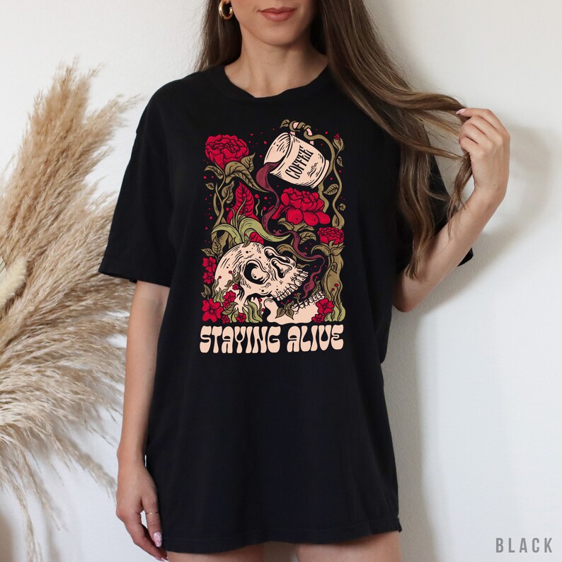 May include: Black t-shirt with a graphic of a skull with coffee pouring into its mouth, surrounded by red roses and vines. The text "STAYING ALIVE" is printed below the skull.