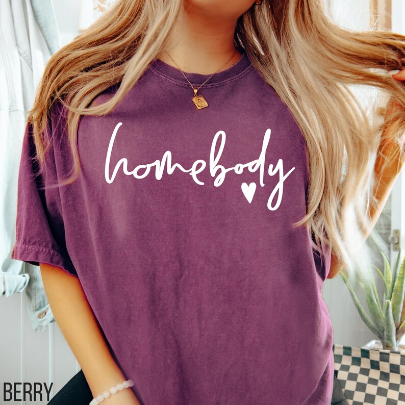 Puede incluir: Una camiseta morada con el texto "homebody" en letras blancas con un peque&ntilde;o coraz&oacute;n blanco.