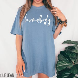 Puede incluir: Una camiseta de gran tama&ntilde;o de color azul jean con el texto "homebody" en letras blancas y un peque&ntilde;o coraz&oacute;n.