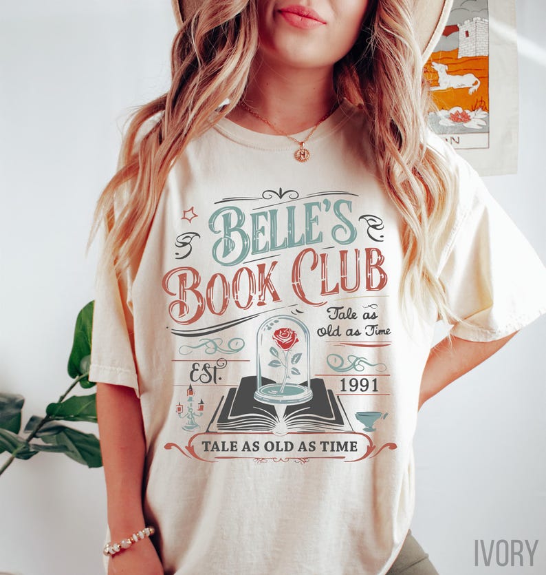 May include: Ivory-colored t-shirt with a graphic design for Belle's Book Club. The design includes text, a rose in a glass dome, and the phrase "Tale as old as Time." The shirt also has the year "1991" printed on it.