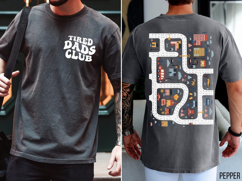 K&ouml;nnte beinhalten: Pfeffergraues T-Shirt mit dem wei&szlig;en Schriftzug "TIRED DADS CLUB" auf der Vorderseite. Auf der R&uuml;ckseite befindet sich ein farbenfrohes Stra&szlig;enkarten-Design mit Autos und Geb&auml;uden. Das Shirt hat eine lockere Passform.