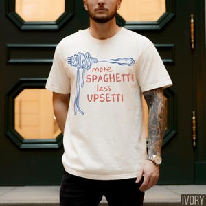 May include: A white t-shirt with a blue and red graphic of spaghetti noodles and the text "more spaghetti less upsetti".