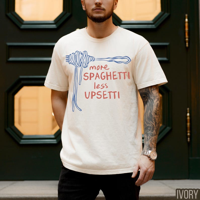 May include: A white t-shirt with a blue and red graphic of spaghetti noodles and the text "more spaghetti less upsetti".