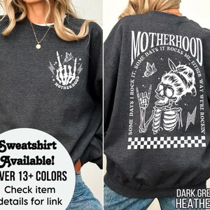 May include: Dark grey heather sweatshirt with a white graphic of a skeleton with a butterfly and the text "MOTHERHOOD SOME DAYS I ROCK IT. SOME DAYS IT ROCKS ME. EITHER WAY WE'RE ROCKIN'."