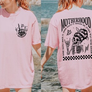 May include: Pink t-shirt with a black skeleton graphic and the text "MOTHERHOOD SOME DAYS I ROCK IT. SOME DAYS IT ROCKS ME, EITHER WAY WE'RE ROCKIN'" on the back. The front of the shirt has a smaller black skeleton hand graphic with the word "MOTHERHOOD" underneath.