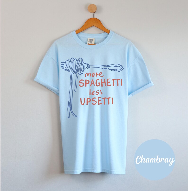 May include: Light blue t-shirt with a blue and red graphic of spaghetti on a fork. The text on the shirt reads "more spaghetti less upsetti".