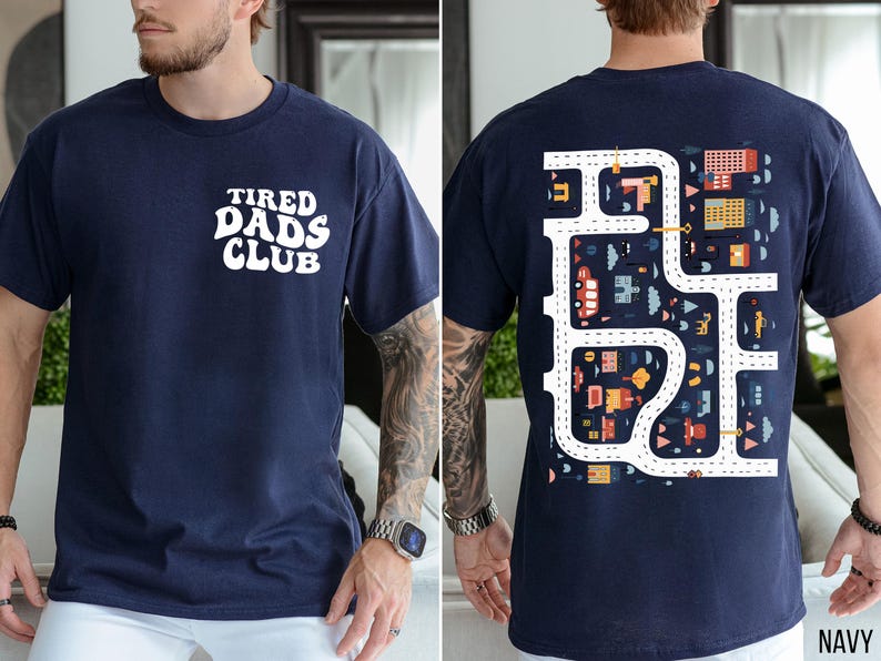 K&ouml;nnte beinhalten: Marineblaues T-Shirt mit dem Text "TIRED DADS CLUB" auf der Vorderseite. Die R&uuml;ckseite des Shirts zeigt ein farbenfrohes Stra&szlig;enkarten-Design mit Autos, Geb&auml;uden und B&auml;umen. Das Shirt ist ein bequemer, l&auml;ssiger Stil.