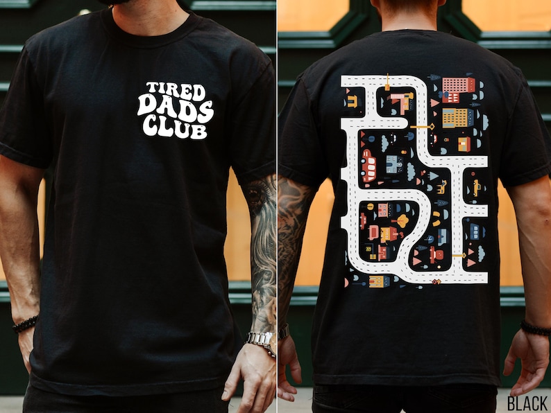 K&ouml;nnte beinhalten: Schwarzes T-Shirt mit dem wei&szlig;en Text "TIRED DADS CLUB" auf der Vorderseite. Die R&uuml;ckseite zeigt ein farbenfrohes Stra&szlig;enkarten-Design mit Geb&auml;uden, Autos und B&auml;umen. Ein l&auml;ssiges, bequemes T-Shirt.