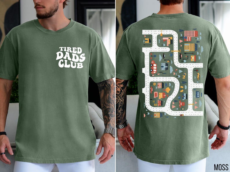 K&ouml;nnte beinhalten: Moosgr&uuml;nes T-Shirt mit dem wei&szlig;en Schriftzug "TIRED DADS CLUB" auf der Vorderseite. Die R&uuml;ckseite zeigt ein Stra&szlig;enkarten-Design mit Autos, Geb&auml;uden und B&auml;umen. Das Shirt ist ein bequemer, l&auml;ssiger Stil.