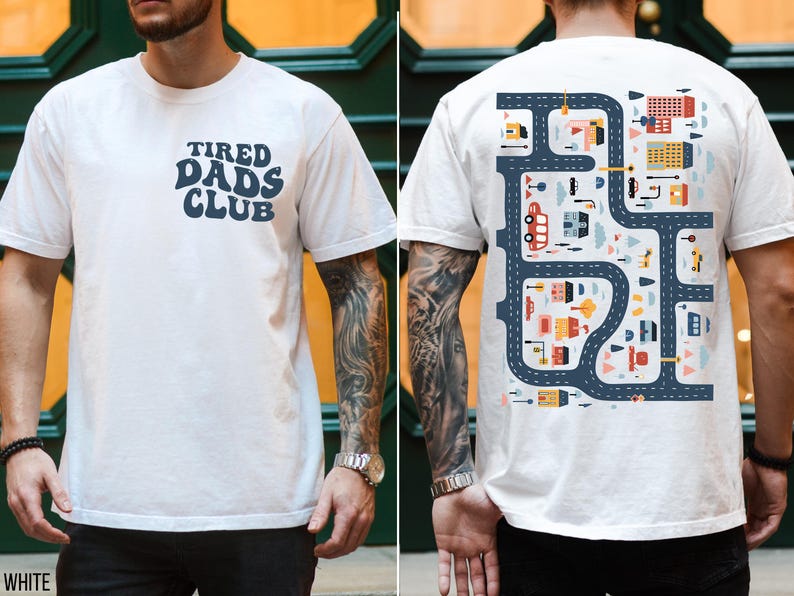 K&ouml;nnte beinhalten: Wei&szlig;es T-Shirt mit "TIRED DADS CLUB" in Marineblau auf der Vorderseite. Die R&uuml;ckseite zeigt ein farbenfrohes Stra&szlig;enkarten-Design mit Geb&auml;uden, Autos und B&auml;umen. Ein l&auml;ssiges T-Shirt mit kurzen &Auml;rmeln.