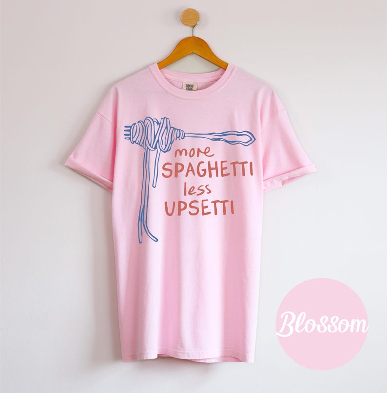 May include: Pink t-shirt with a blue and orange illustration of spaghetti on a fork and the text "more spaghetti less upsetti".
