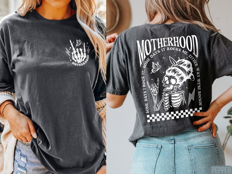 May include: A black t-shirt with a white graphic print on the front and back. The front graphic is a skeleton hand with a lightning bolt and the word 'MOTHERHOOD'. The back graphic is a skeleton with a butterfly and the text 'MOTHERHOOD SOME DAYS I ROCK IT. SOME DAYS IT ROCKS ME. EITHER WAY WE'RE ROCKIN''.