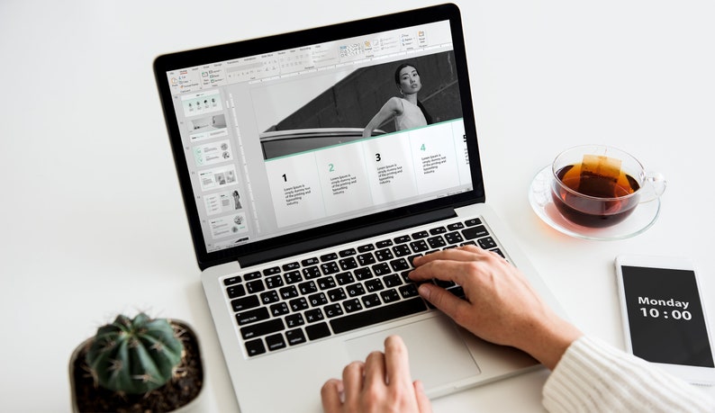May include: A person working on a laptop computer with a presentation open on the screen. The presentation has four sections with numbers 1 through 4. The presentation includes a black and white photo of a person standing next to a car. The laptop is on a white desk with a cactus plant, a cup of tea, and a smartphone with the time 10:00 and the word "Monday" displayed.