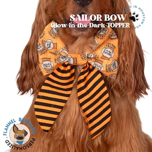 Può includere: Un fiocco da marinaio a righe arancioni e nere con la scritta "I SEE MANY TREATS IN MY FUTURE" e "SAILOR BOW Glow in the Dark TOPPER" stampata sopra. Il fiocco è su un cane.