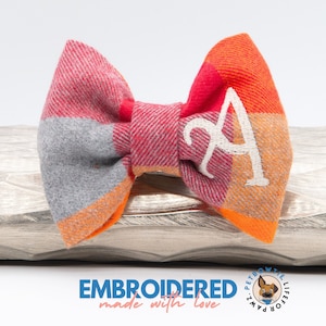 May include: A red, orange and grey plaid bow tie with a white embroidered letter "A".